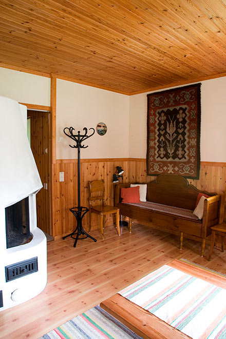 Saunatuvan oleskelutilassa puinen sohva, takka, naulakko, tuoli ja seinäryijy