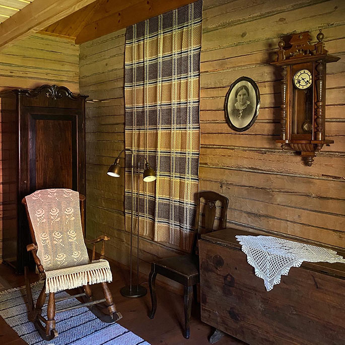 Hirsiaitan sisätilat, jossa keinutuoli, puinen arkku, kaappikello ja kaappi